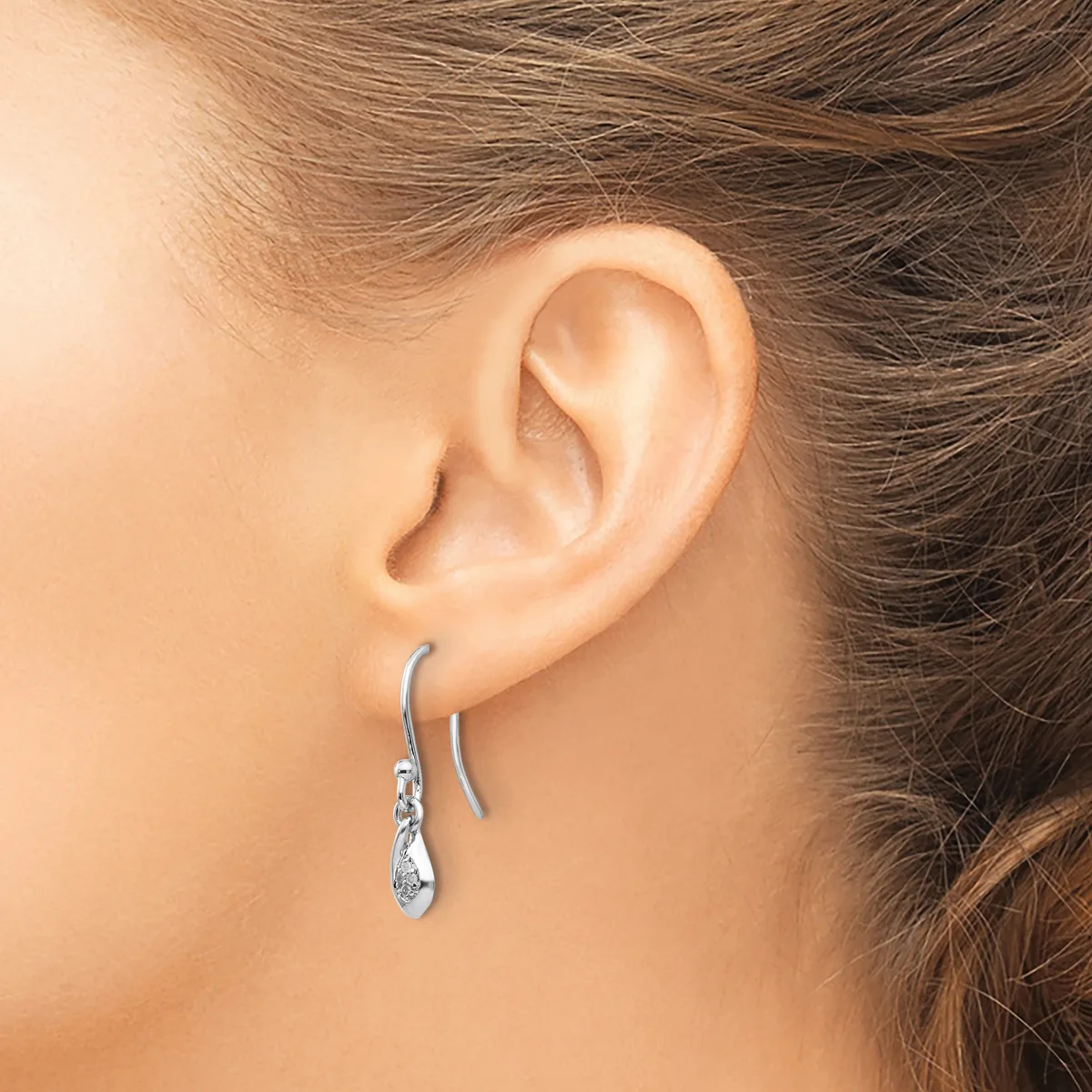 A woman wearing silver teardrop-shaped earrings with textured details, shown from the side profile displaying her ear and part of her face and hair.