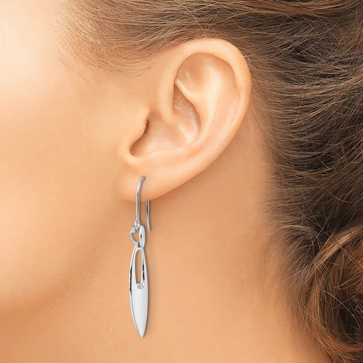 A woman wearing silver drop earrings with elongated oval pendants hanging from hook-style ear wires.