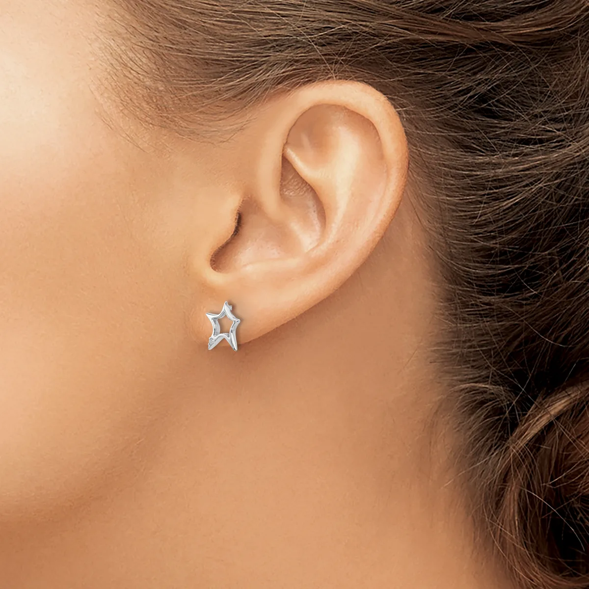 A person wearing a small star-shaped silver earring with a textured finish in their earlobe.