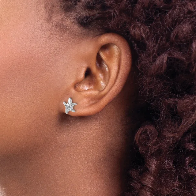 A close-up side view of a person's ear wearing a small star-shaped stud earring in silver or white metal.