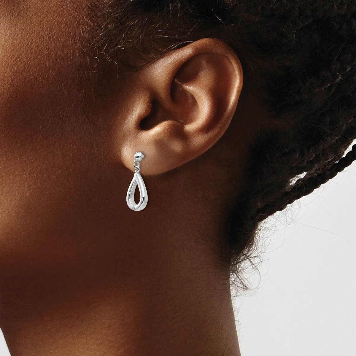 A person wearing a teardrop-shaped silver dangle earring with a small round stone at the top, shown from the side view of their ear and neck.