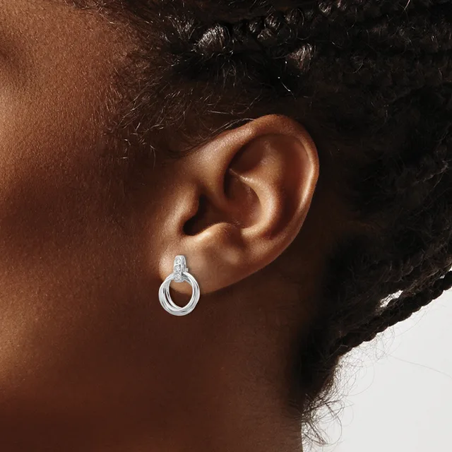 A close-up of a person's ear wearing a small silver hoop earring with a textured surface and post back.