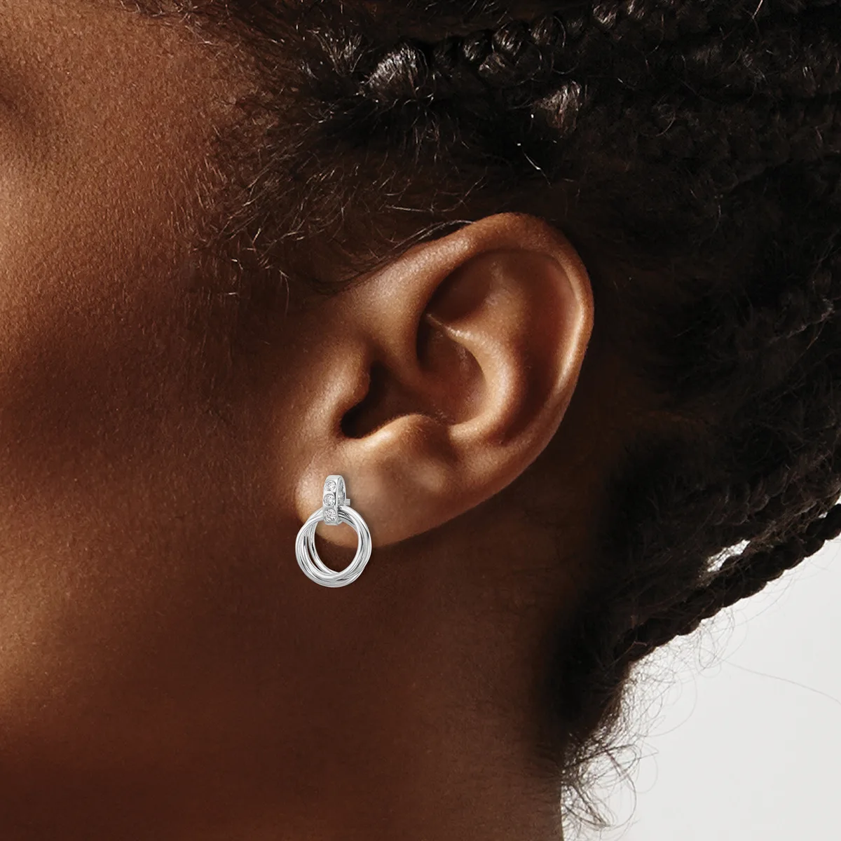 A close-up of a person's ear wearing a small silver hoop earring with a textured surface and post back.