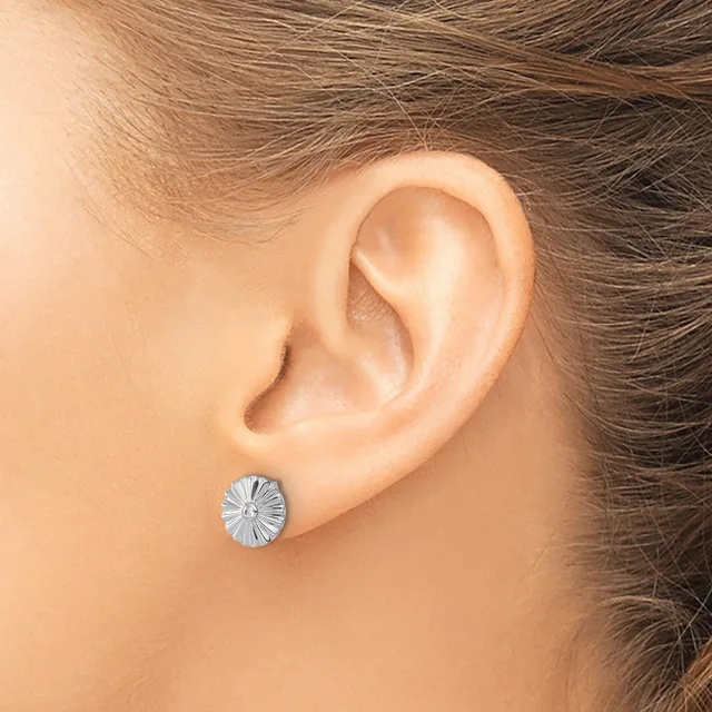 A silver oval stud earring with radiating linear texture sits in the earlobe of a person with brown hair.