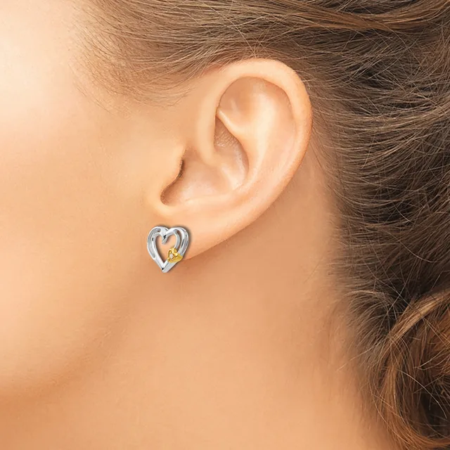 A person wearing a two-tone heart-shaped earring with silver and gold accents displayed on their earlobe.
