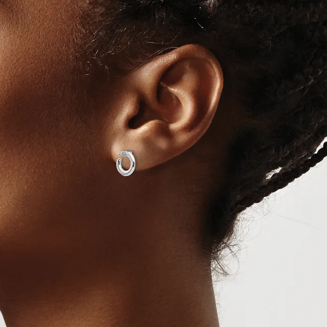 A close-up view of a person's ear wearing a small polished silver oval hoop earring.