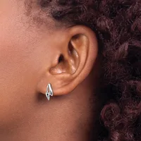 A person with brown skin and dark curly hair wears a pair of silver teardrop-shaped hoop earrings on their pierced earlobes.