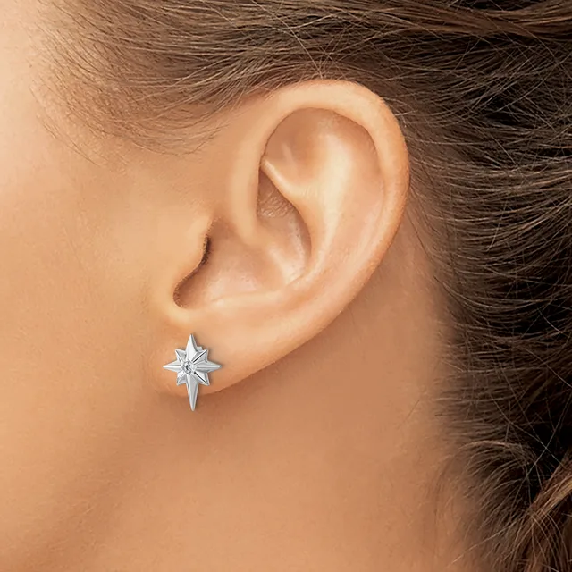 A person wearing a four-pointed star earring in silver metal on their earlobe.