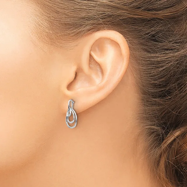 A woman wearing small silver oval hoop earrings with a textured finish, shown from the side profile of her head and ear.