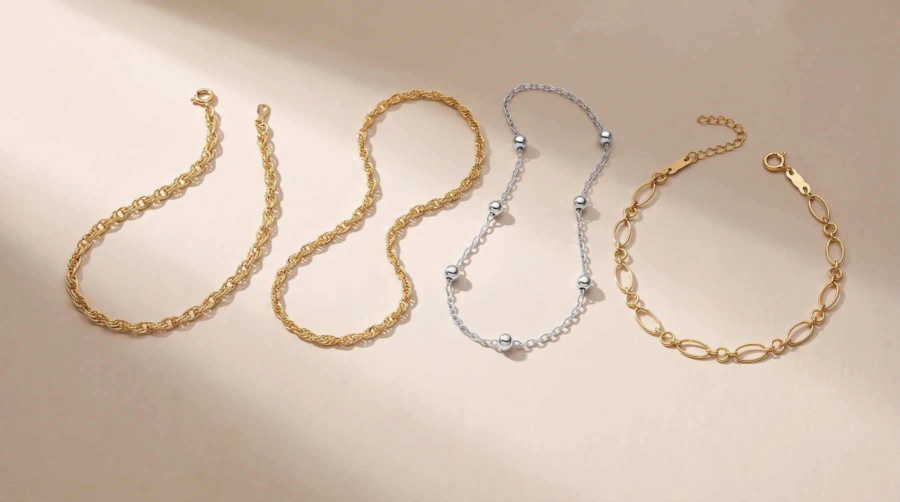 Six gold and silver chain necklaces and bracelets arranged in rows on a beige surface, including textured links, beaded designs, and oval-link styles.