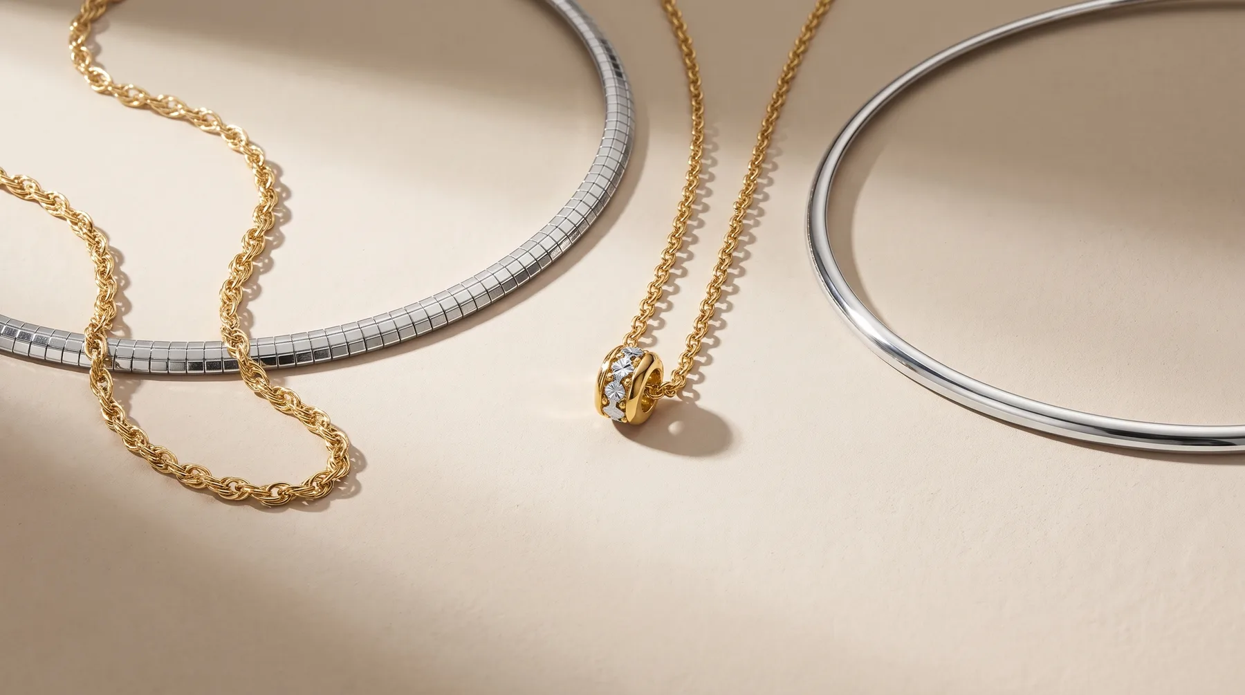 Gold and silver chain necklaces and bracelets arranged on a beige surface, displaying various link styles and finishes.