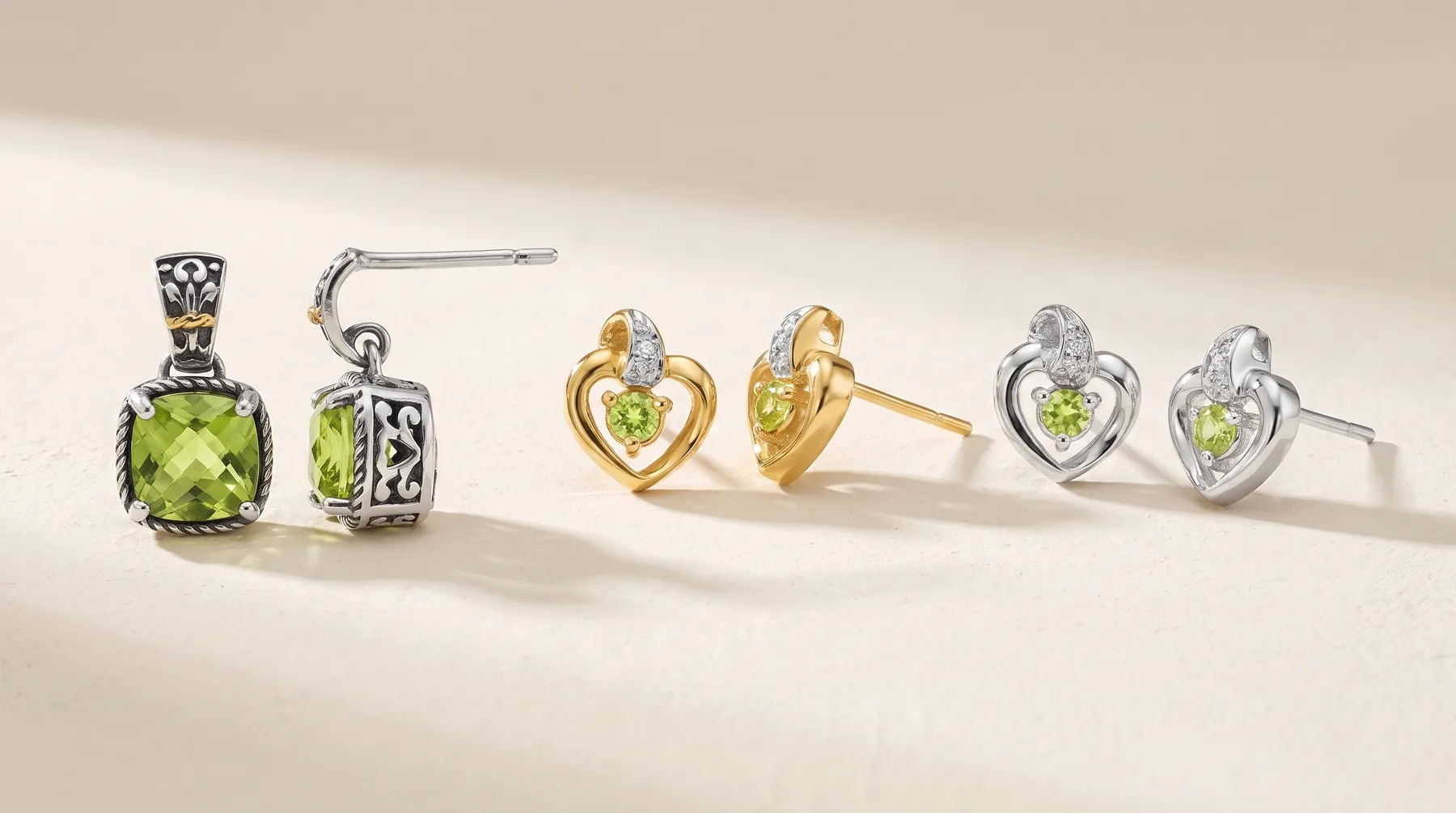 Three pairs of gemstone jewelry displayed on a neutral surface: silver drop earrings with green cushion stones, gold heart-shaped stud earrings with green stones, and silver heart stud earrings with green stones.