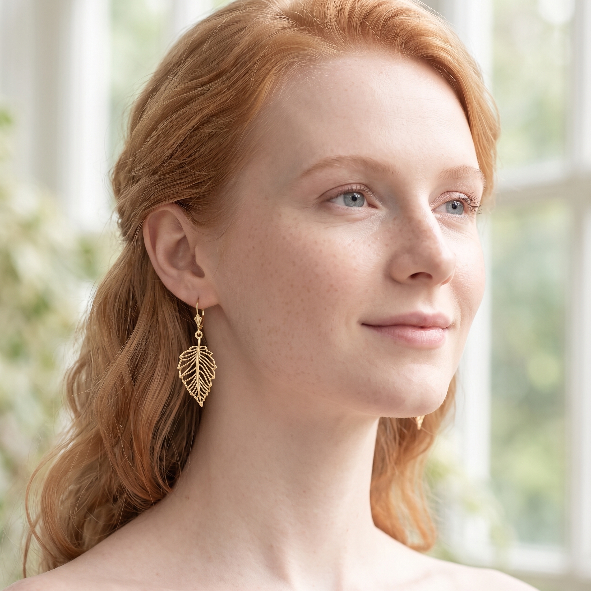 Model in soft morning light wearing gold open leaf dangle earrings