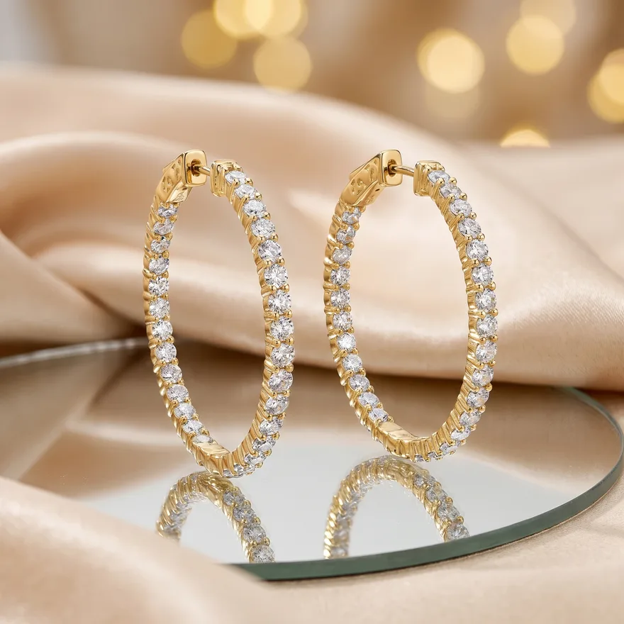 Pair of gold moissanite hoop earrings standing side by side on a mirrored tray against champagne silk and golden bokeh