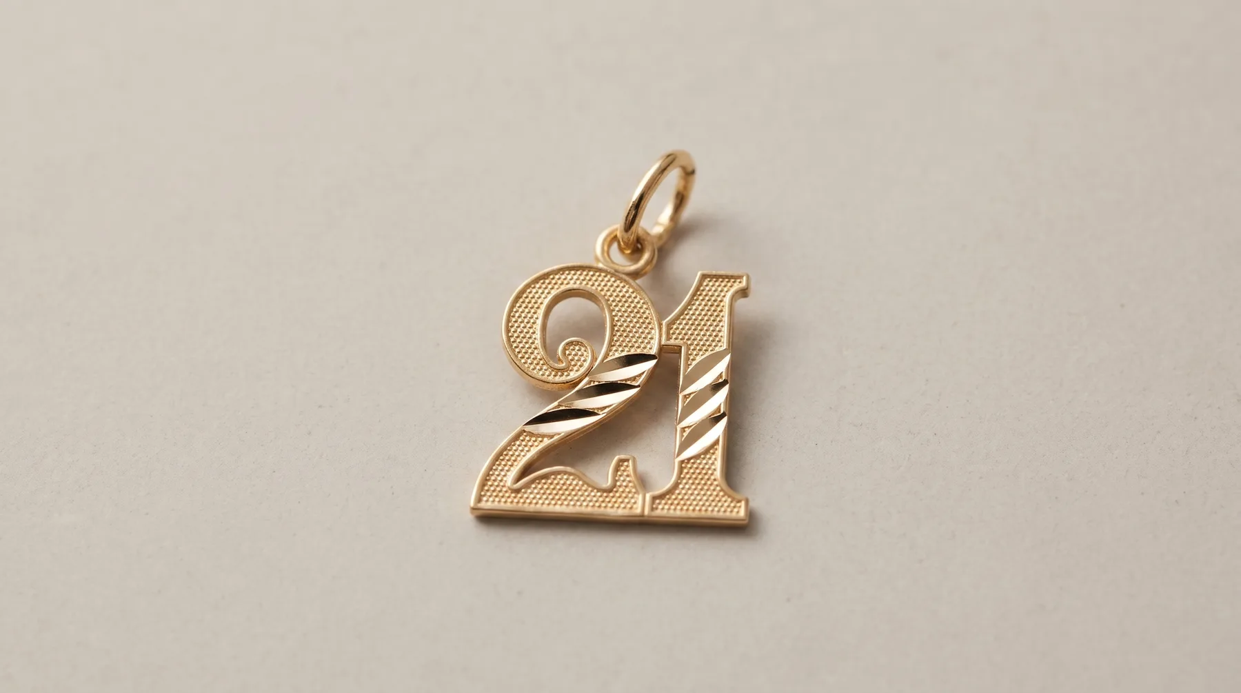 Gold pendant charm shaped like the number 21 with diagonal stripe detailing, suspended from a small loop, displayed against a neutral background.