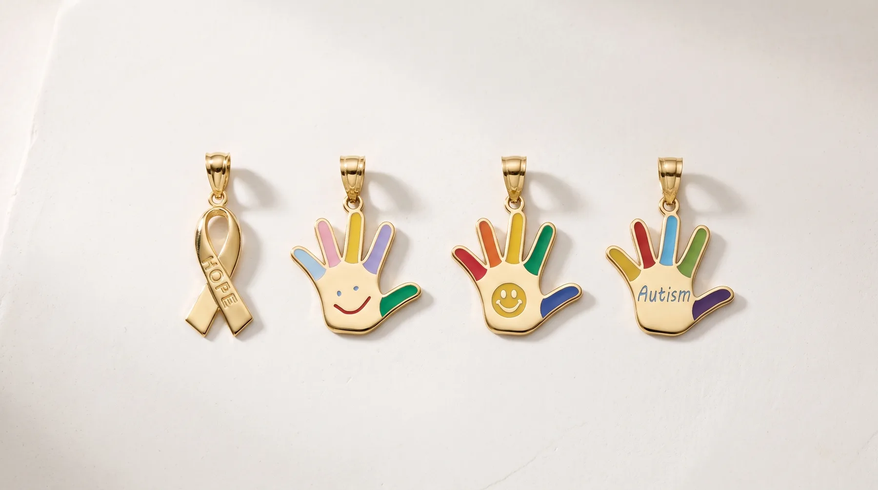 Four gold pendant charms displayed in a row: a ribbon, and three hand designs with colorful enamel fingers and various symbols including a smiley face and text.