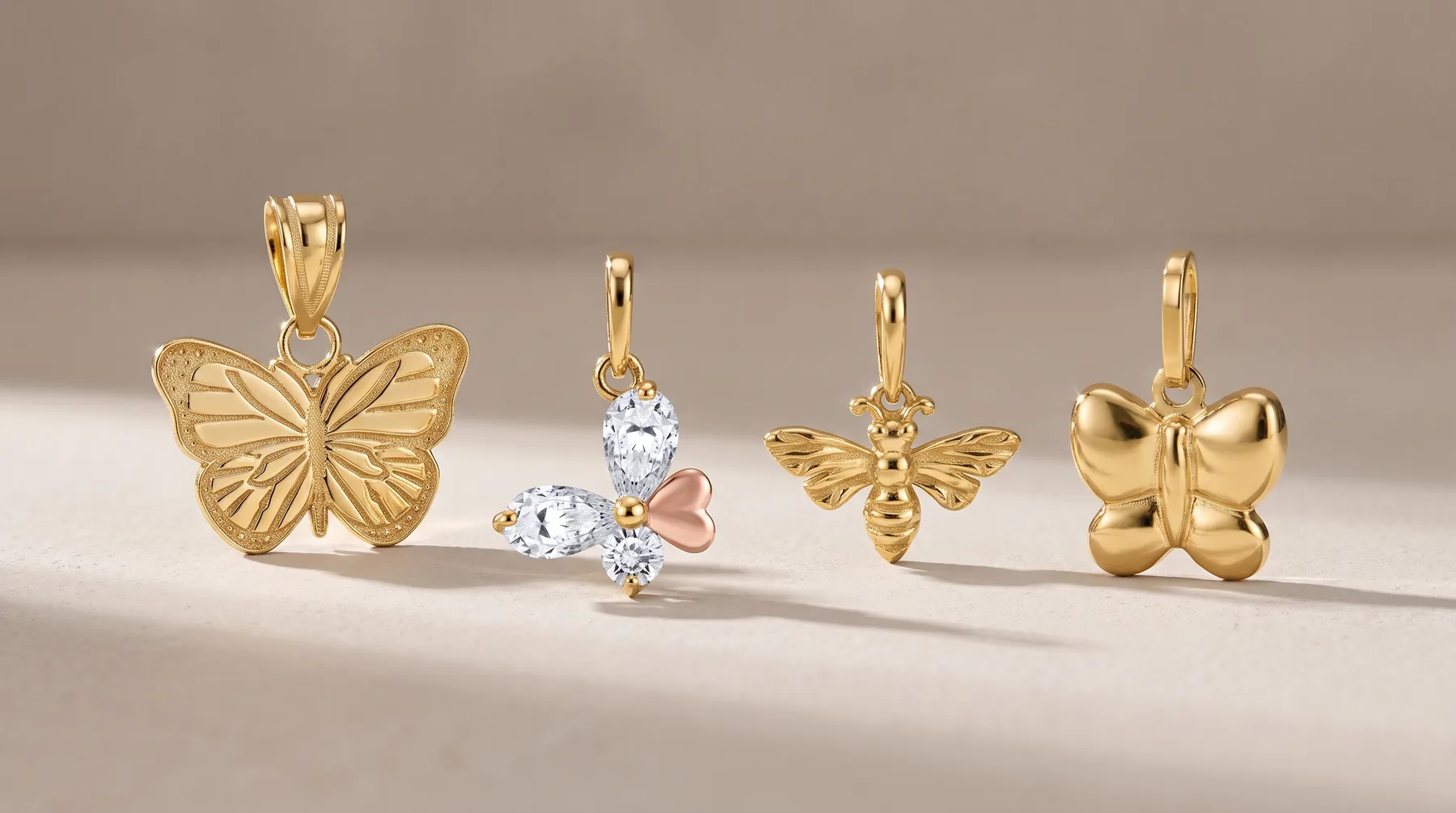 Four gold butterfly and insect pendant charms displayed in a row, featuring textured and polished finishes with some set with white and pink gemstones.