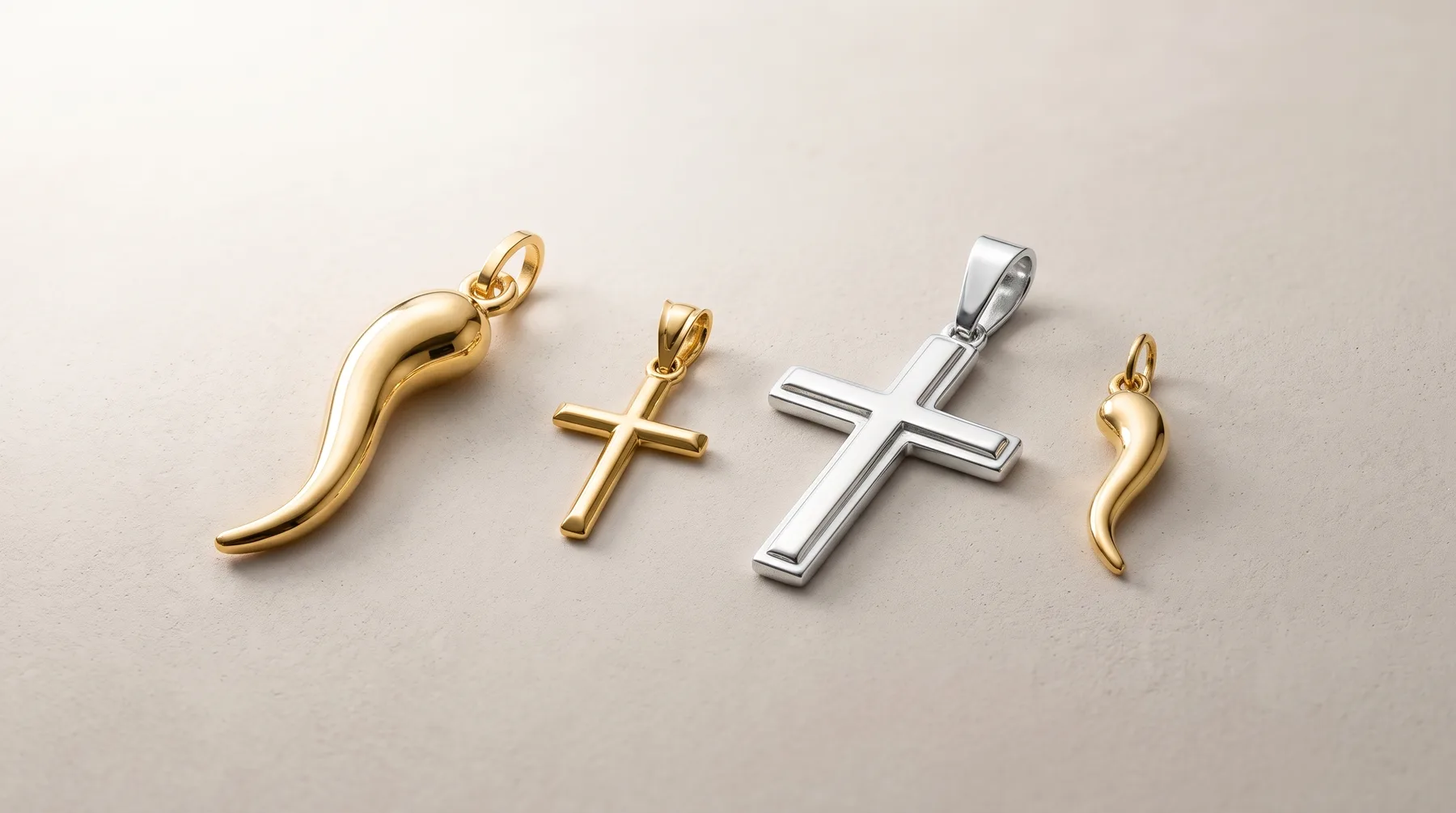 Four metal pendants arranged in a row on a neutral background: a curved gold horn shape, a small gold cross, a larger silver cross, and a small gold horn shape.