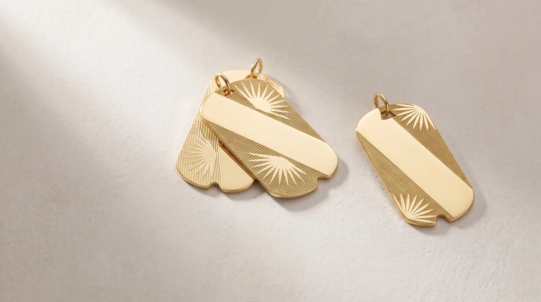 Two gold pendant charms with fan-shaped designs and textured surfaces, one larger with multiple lobes and one smaller, displayed on a white surface.