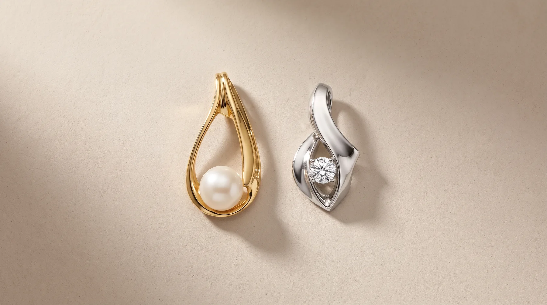 Two teardrop-shaped pendant necklaces displayed against a neutral background: one in yellow gold with a pearl, one in white metal with a faceted diamond.