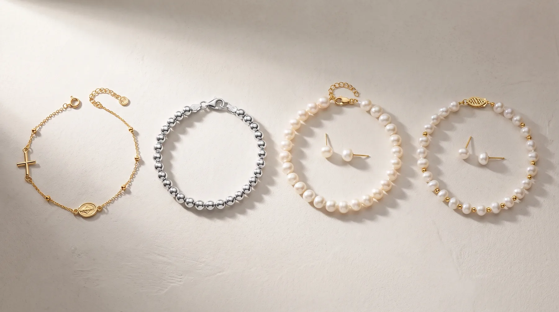 Four beaded bracelets arranged in a row: a gold-toned bracelet with a cross charm, a silver beaded bracelet, and two pearl bracelets with gold-toned findings and small decorative charms.