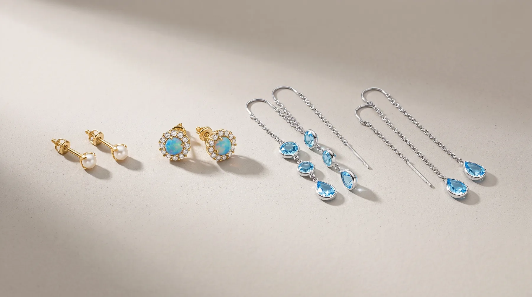 Six pairs of earrings arranged in a row on a white surface, including gold stud pairs with pearls and turquoise stones, and silver threader earrings with blue gemstones.