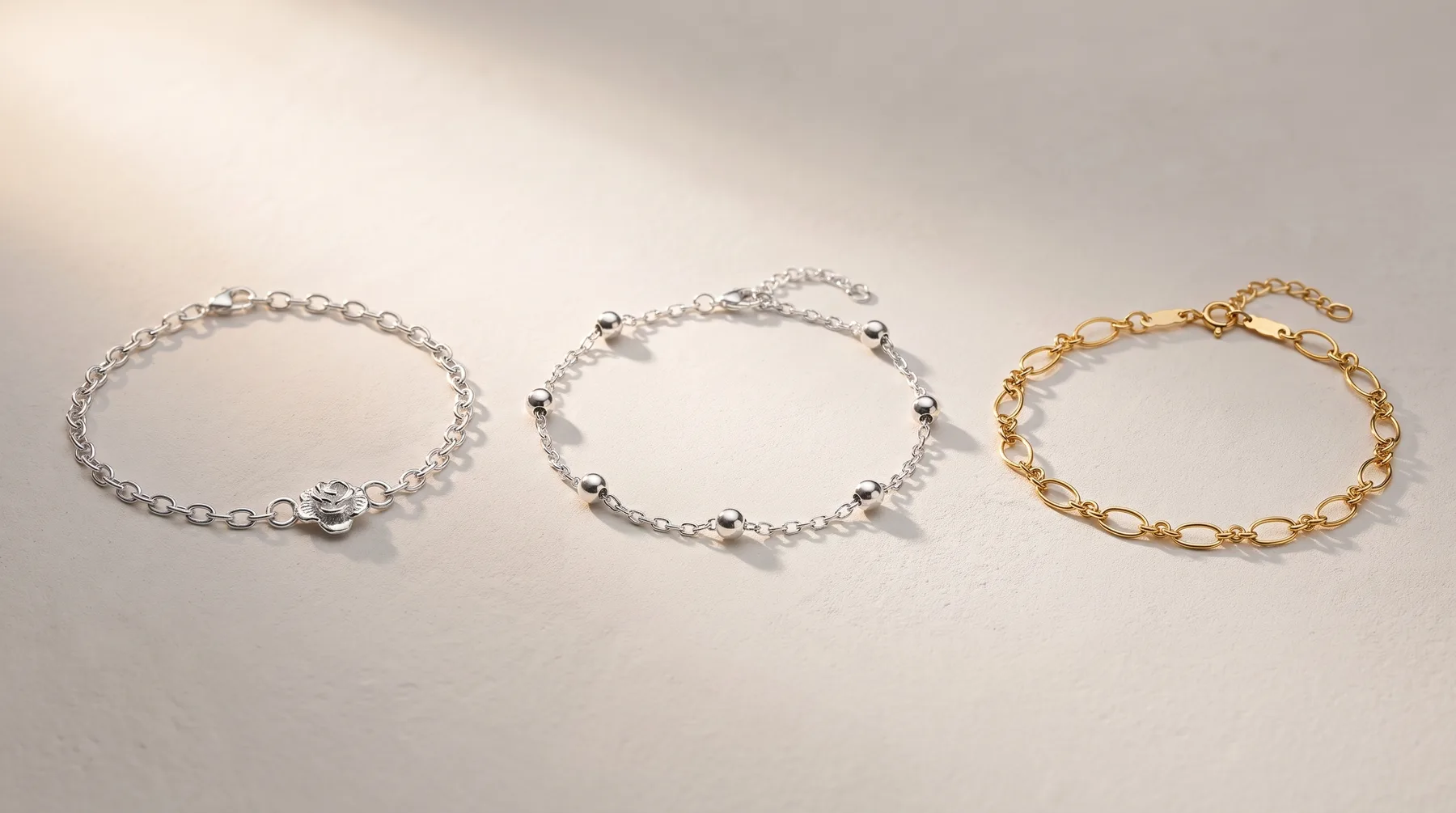 Three delicate chain bracelets arranged in a row: two silver-toned with decorative beads, and one gold-toned with larger oval links.