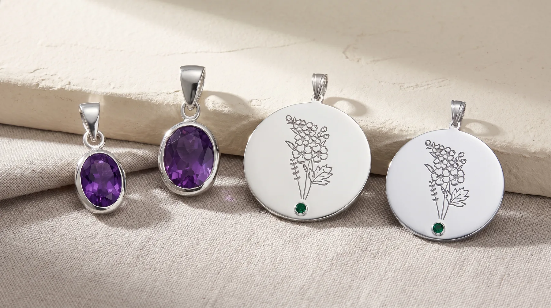 Five silver pendant charms arranged in a row: two with oval purple amethyst stones, three circular white discs engraved with delicate botanical designs and small green gemstones.