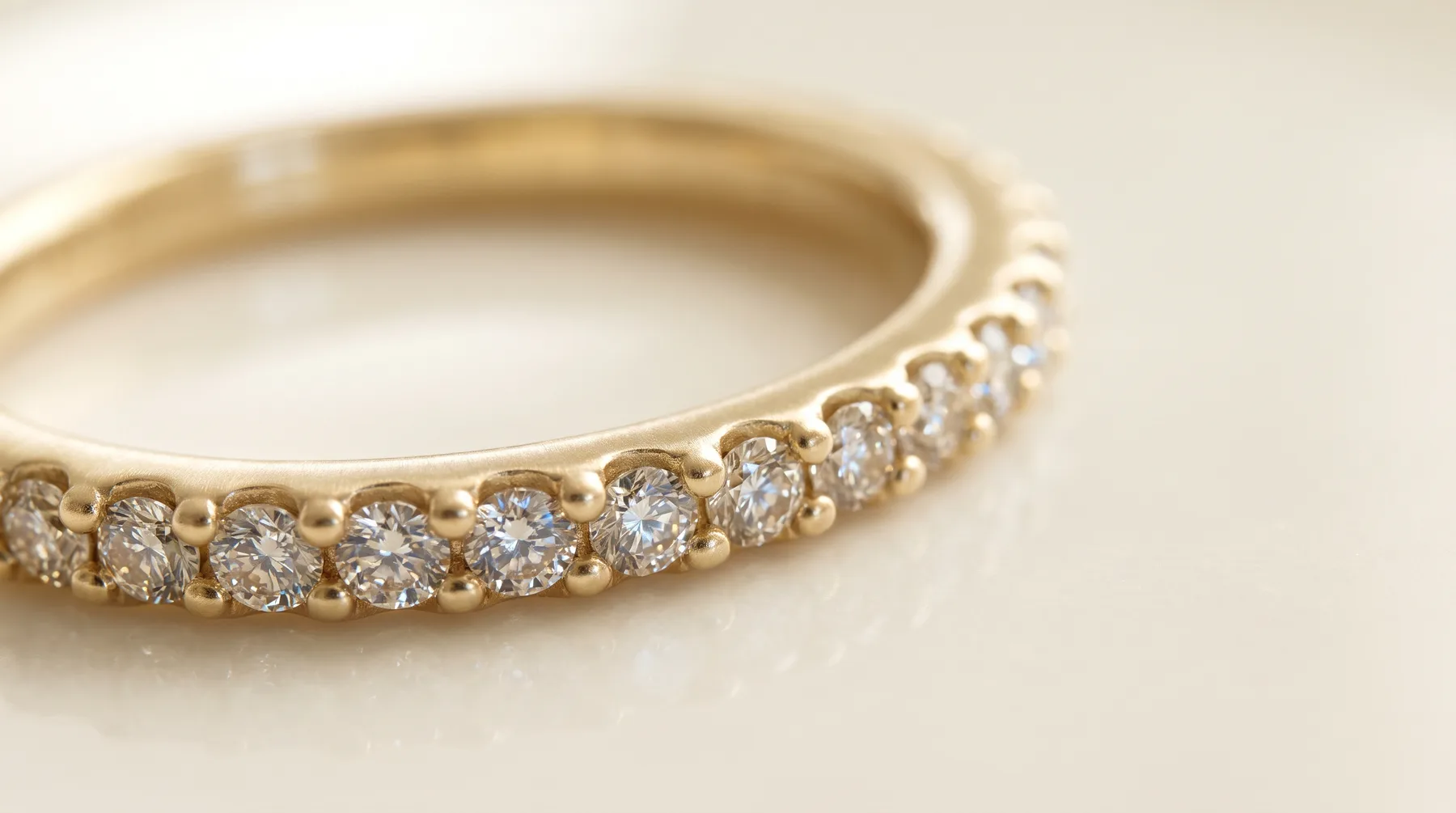Extreme close-up of a yellow gold band set with a row of round diamonds, each held in place by small raised beads of gold.