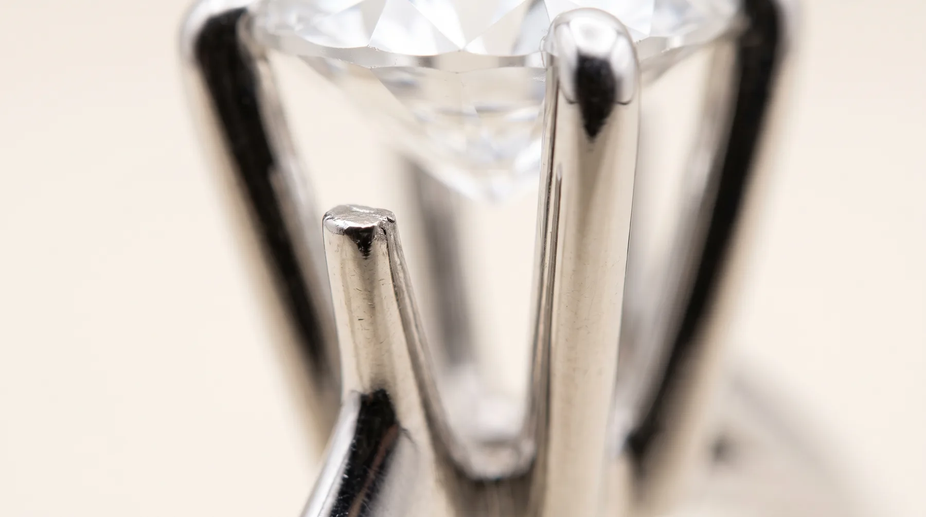 Extreme close view of white metal prongs around a diamond: three prongs fold over the stone's edge while the nearest one is worn short and flat and no longer reaches it