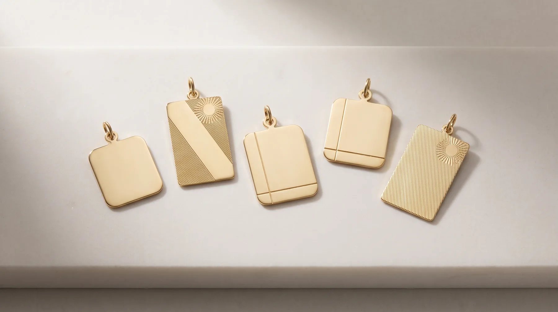 Five gold-toned rectangular pendant charms with various surface finishes including plain, diagonal stripe, vertical lines, and sunburst patterns, each with a small loop at the top.