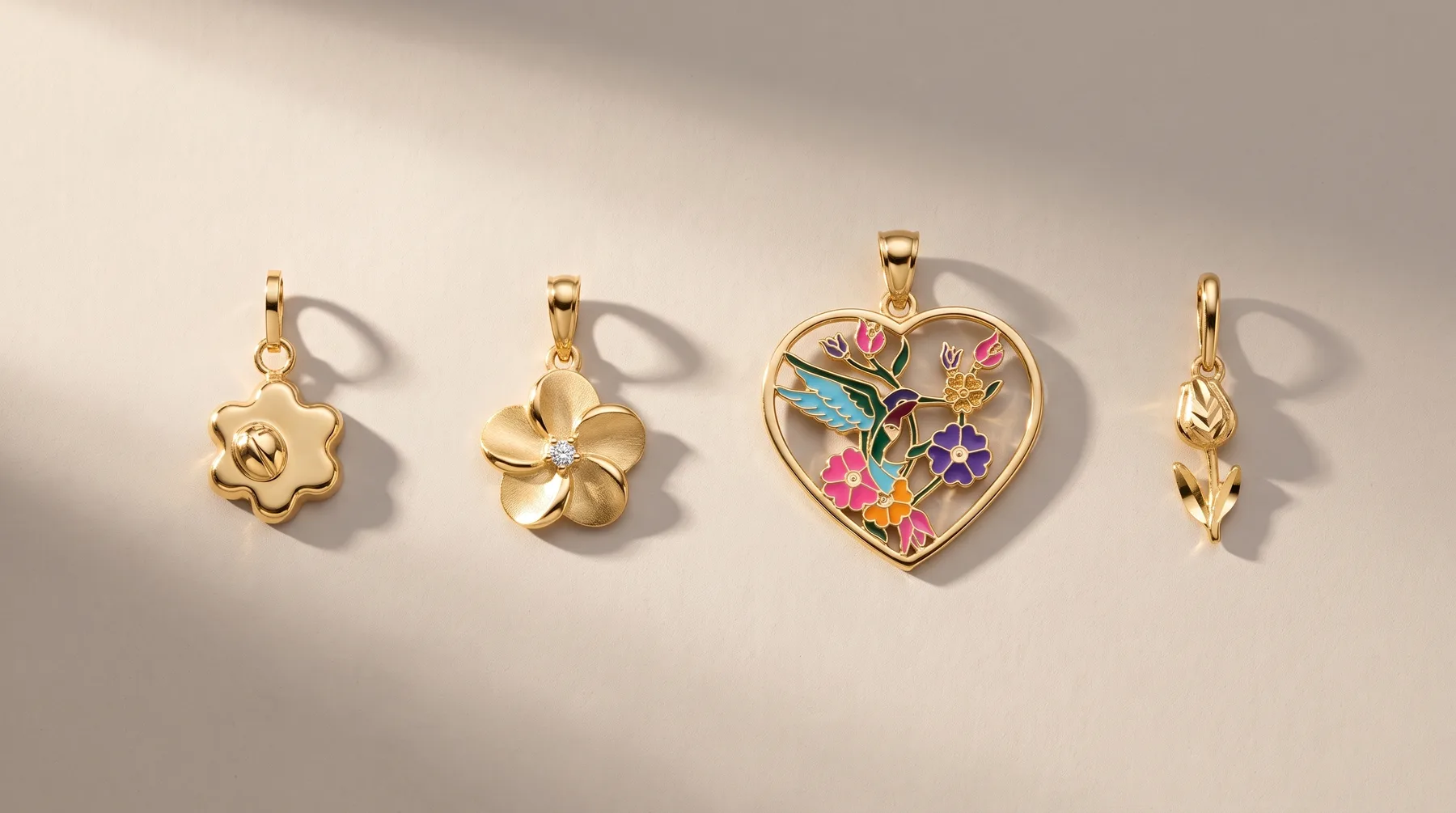 Four gold pendant charms displayed in a row, including a flower with a rose detail, a four-petal flower with a stone center, a heart-shaped locket with colorful enameled flowers and stones, and a leaf-shaped charm, each with a small hallmark.