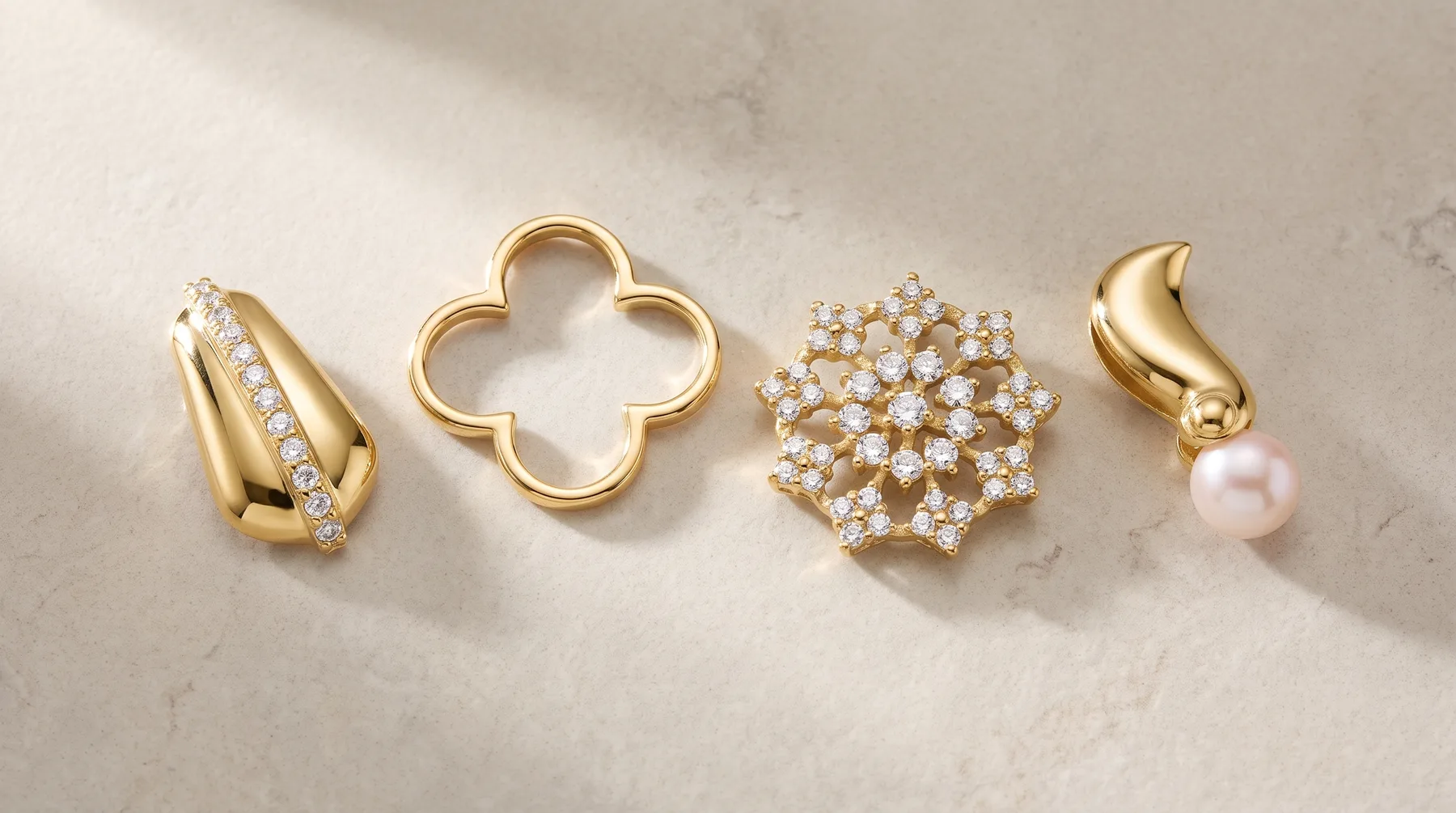 Four gold pendants arranged in a row on a marble surface: a twisted gold piece with diamonds, a four-leaf clover outline, a clustered diamond dome, and a curved gold piece with a pink pearl.