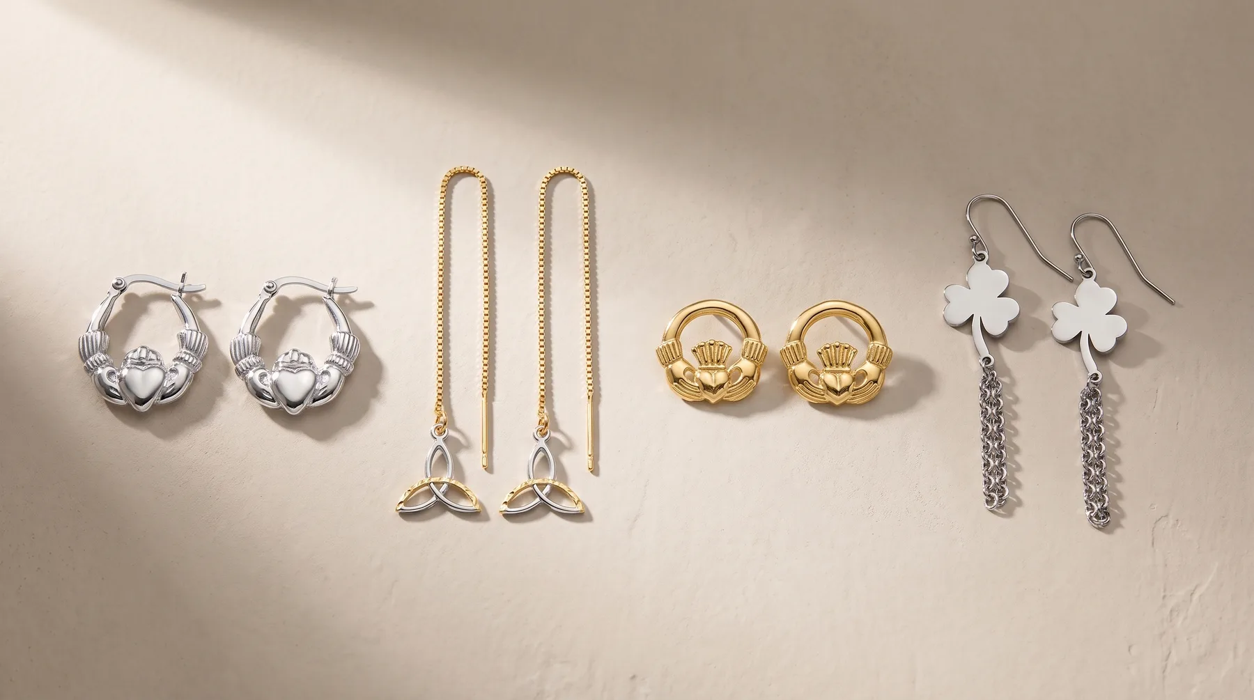 Five pairs of earrings displayed on a neutral background: silver claddagh studs, silver threader earrings with leaf charms, gold claddagh studs, and silver chain drop earrings with white clover charms.