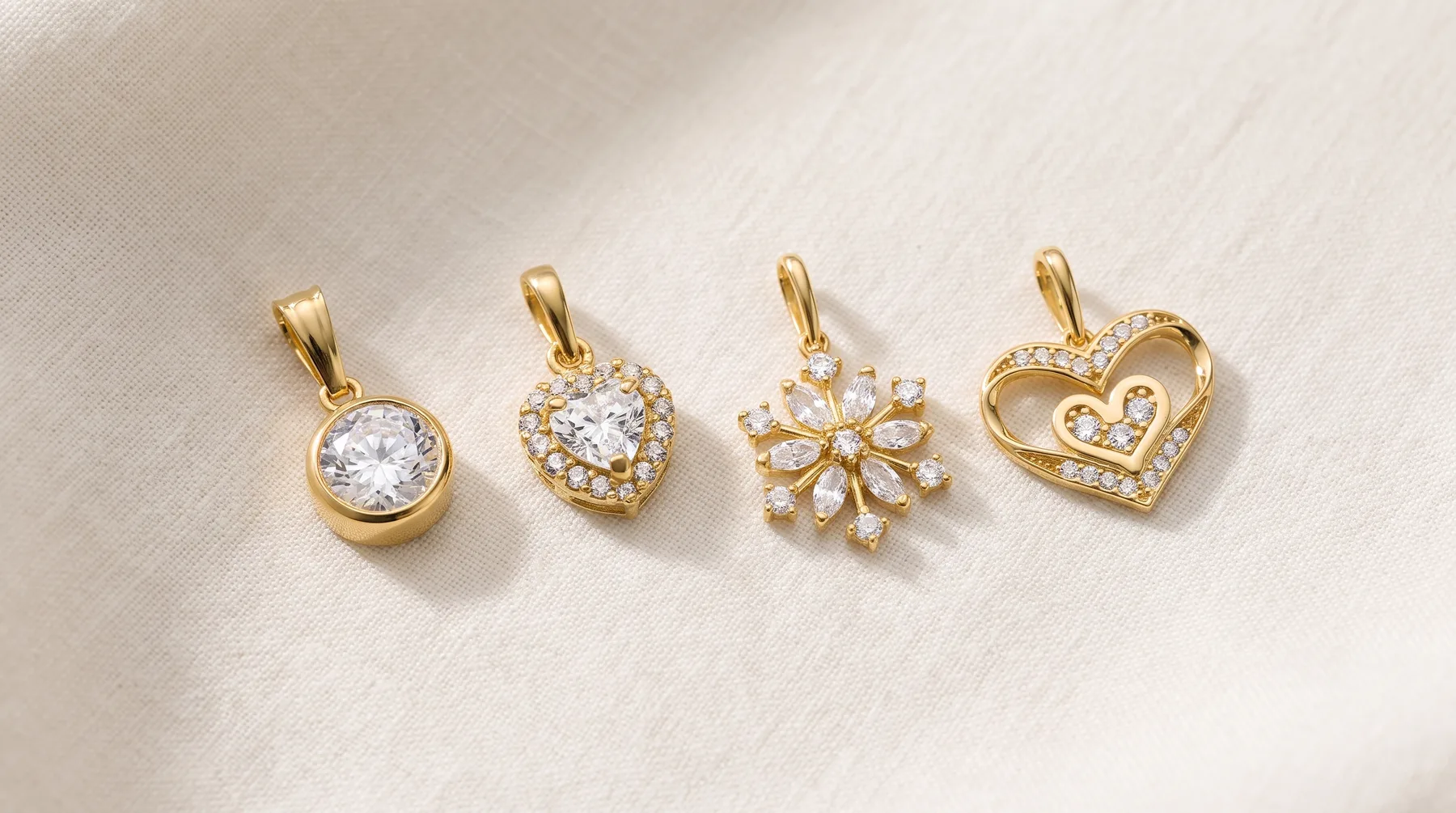 Four gold pendant charms with cubic zirconia stones arranged in a row: a round solitaire, a heart with halo setting, a snowflake or starburst design, and a heart with cutout detail.