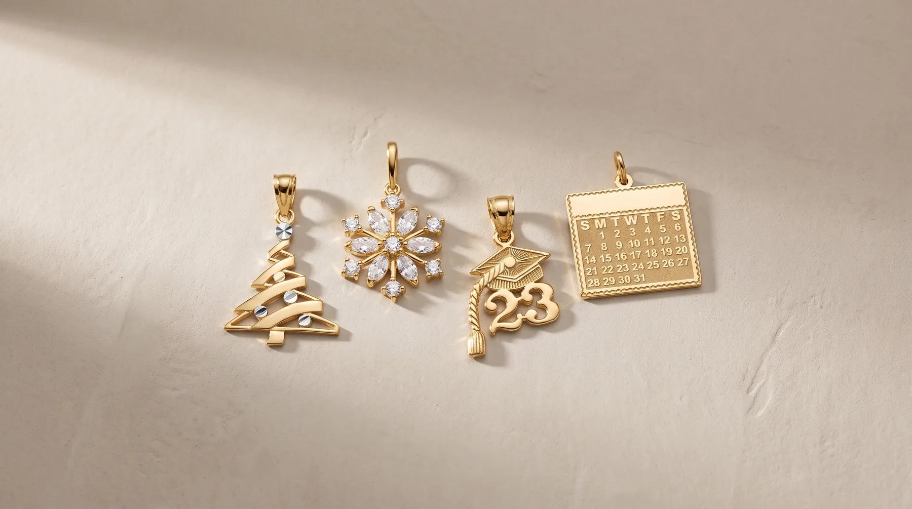 Four gold charm pendants displayed on a white surface: a Christmas tree, a snowflake with crystals, a number 23, and a calendar square, each with a loop for hanging.