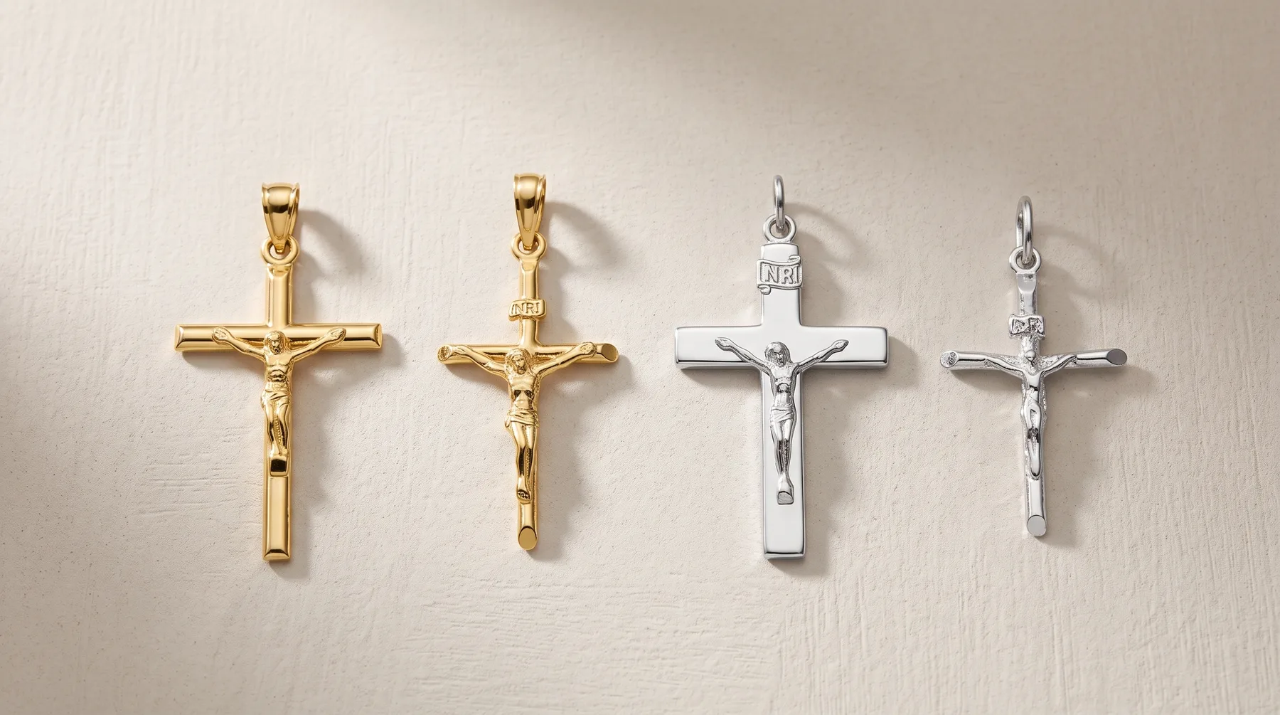 Four religious cross pendants arranged in a row: two gold-toned crucifixes with corpus figures on the left, two silver-toned crucifixes with corpus figures on the right, each with a small loop for chain attachment at the top.