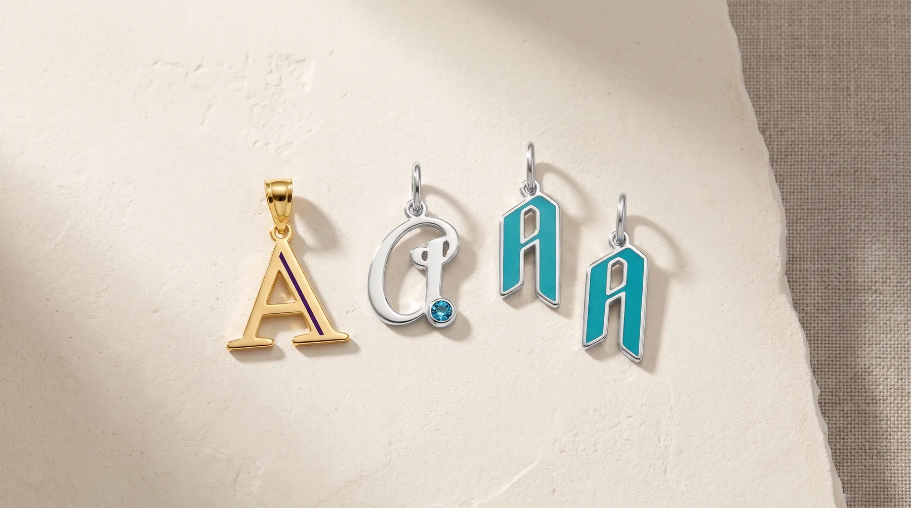 Four letter A pendants displayed on a white surface: one gold-colored solid A, one silver with a small blue stone, and two turquoise enamel A-shaped earrings with silver hooks.