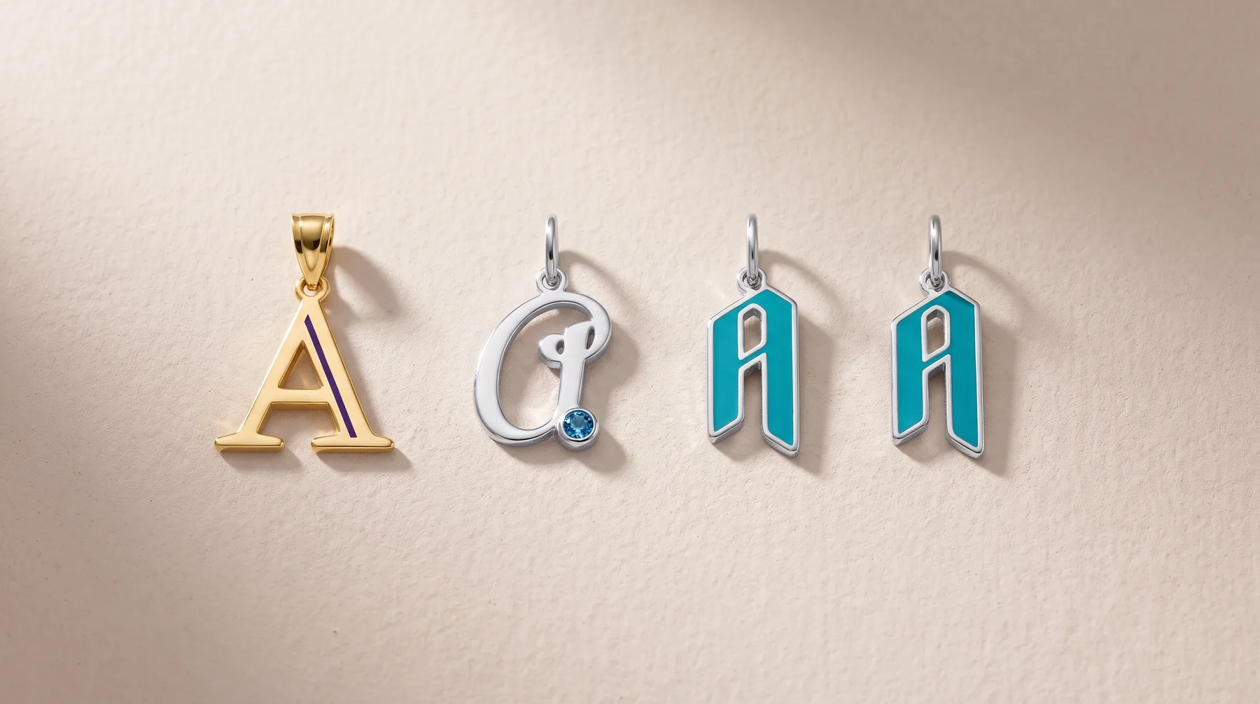Four metal letter pendants displayed in a row: a gold capital A, a silver charm with a gemstone, and two turquoise and silver flag-shaped charms.