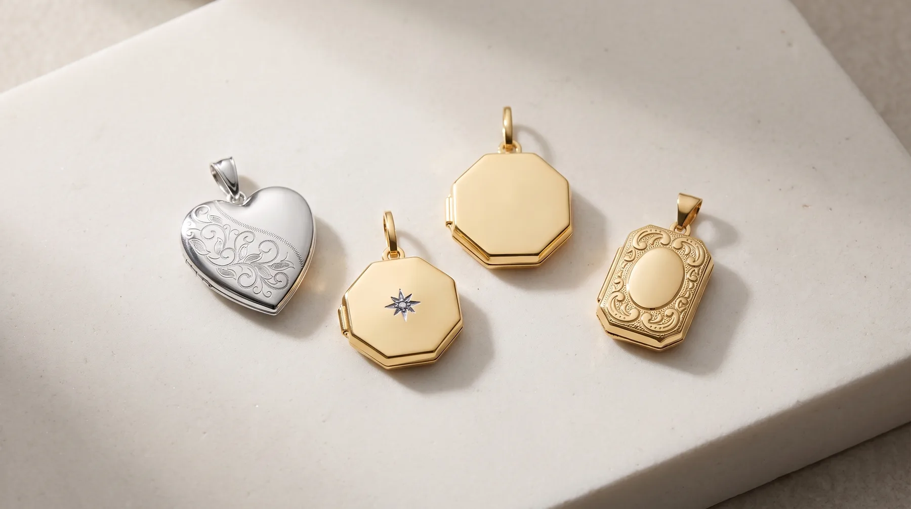 Four gold and silver locket pendants arranged on a white surface, featuring heart and rectangular shapes with decorative engravings and gemstone accents.