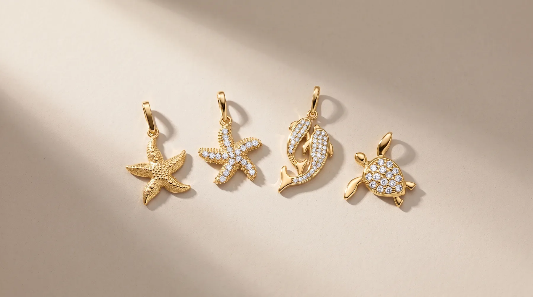 Four gold sea creature charms with bail loops displayed on a neutral background: a textured starfish, a starfish with diamond pave, a curved seahorse, and a turtle with diamond pave details.