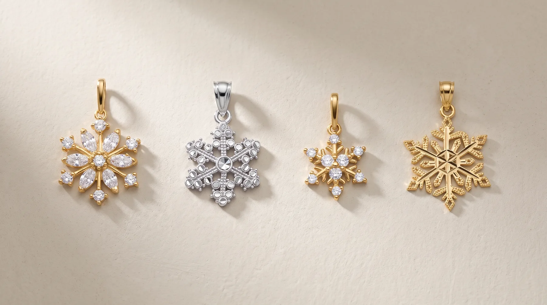 Four snowflake-shaped pendants in gold and silver tones with cubic zirconia stones, arranged in a row against a white background.