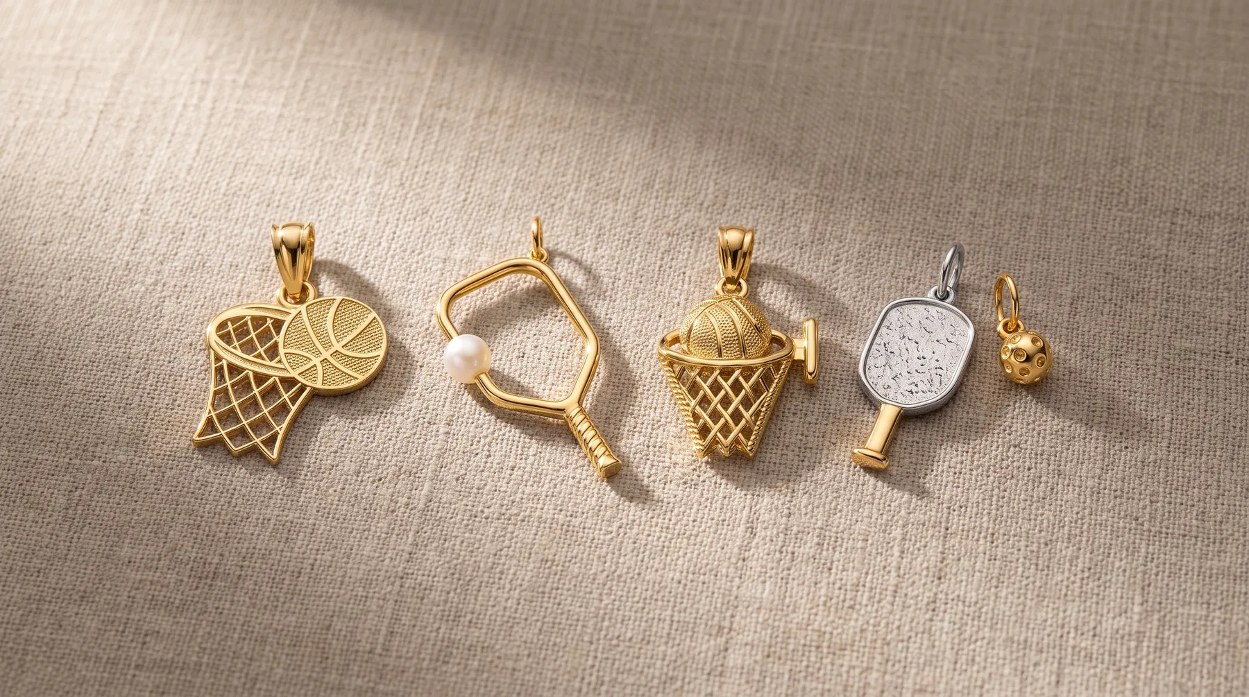 Five gold and silver sports-themed charm pendants arranged in a row, including a basketball hoop, tennis racket, ice cream cone, paddle, and small animal figure.