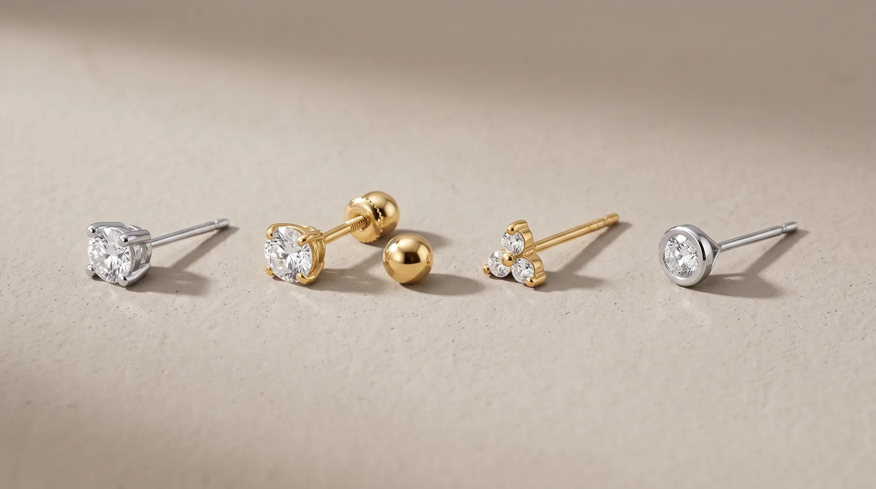 Four diamond stud earrings arranged in a row, featuring round diamonds in white and yellow gold settings with ball post backs.