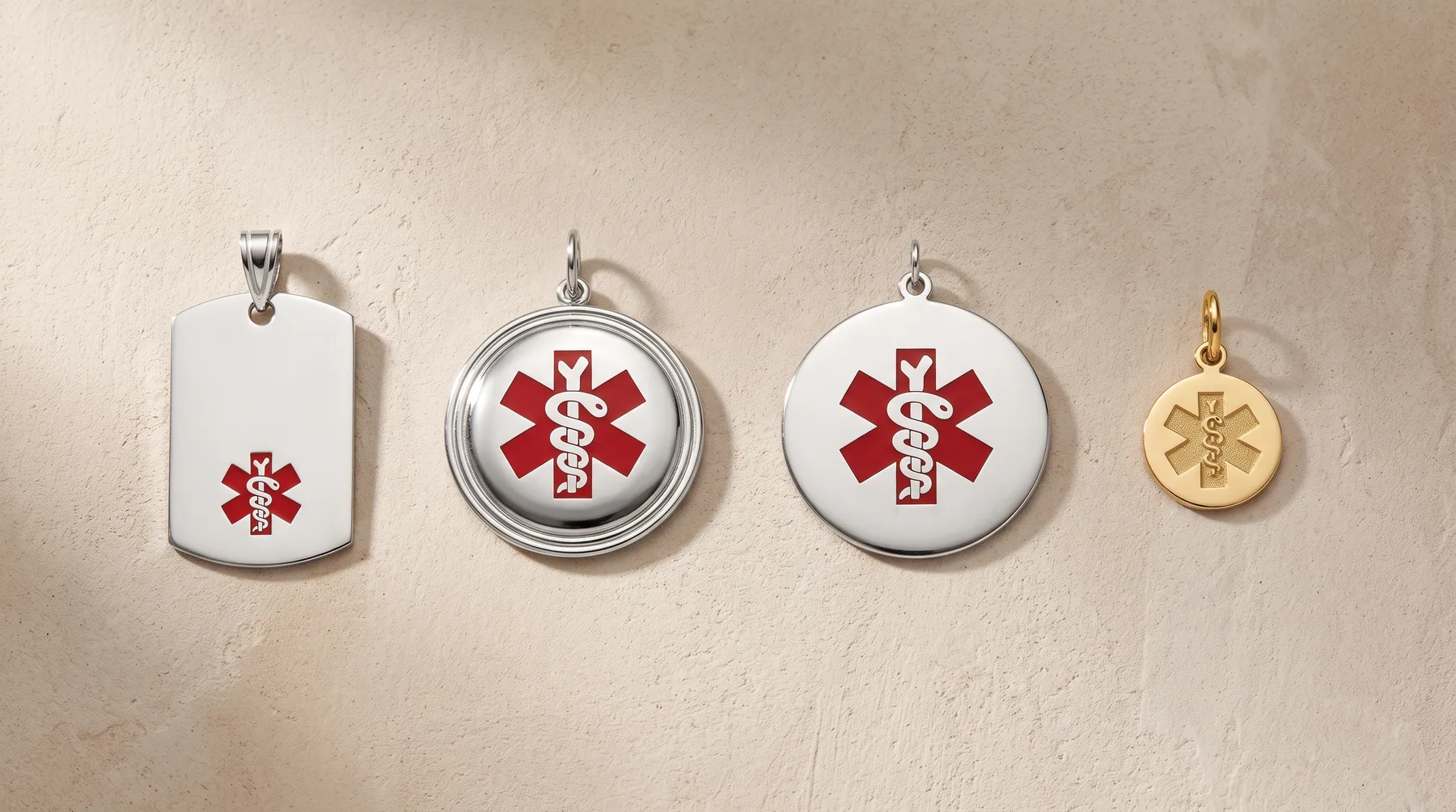 Four medical alert pendants arranged in a row, featuring red and white Star of Life symbols on white and gold-toned metal bases with silver bail loops.