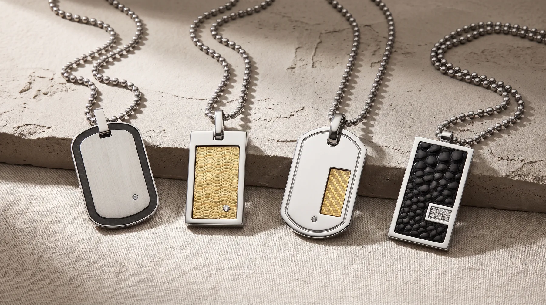 Four rectangular metal dog tag pendants with ball chain necklaces, featuring plain, textured, and patterned surfaces in silver and gold tones.