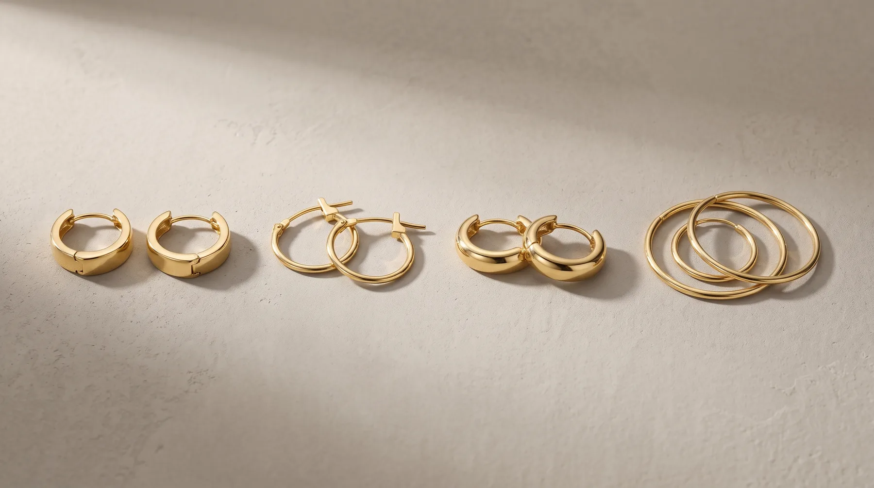 Five pairs of gold hoop earrings in varying thicknesses and sizes arranged in a line on a white surface.