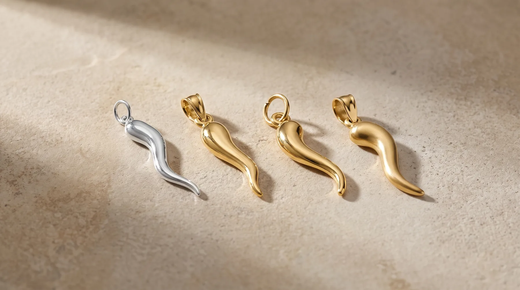 Four curved horn-shaped pendants arranged in a row, one silver and three gold-toned, each with a small loop attachment at the top.