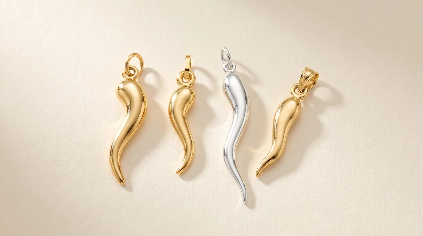 Four curved horn-shaped pendant charms arranged in a row, three in gold finish and one in silver finish, each with a small loop attachment at the top.