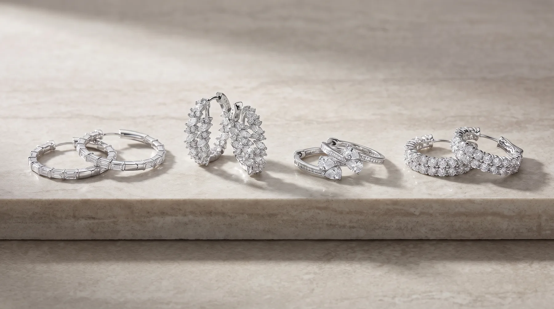 Five diamond and white metal rings displayed in a row on a concrete surface, including solitaire, halo, three-stone, and multi-band styles.